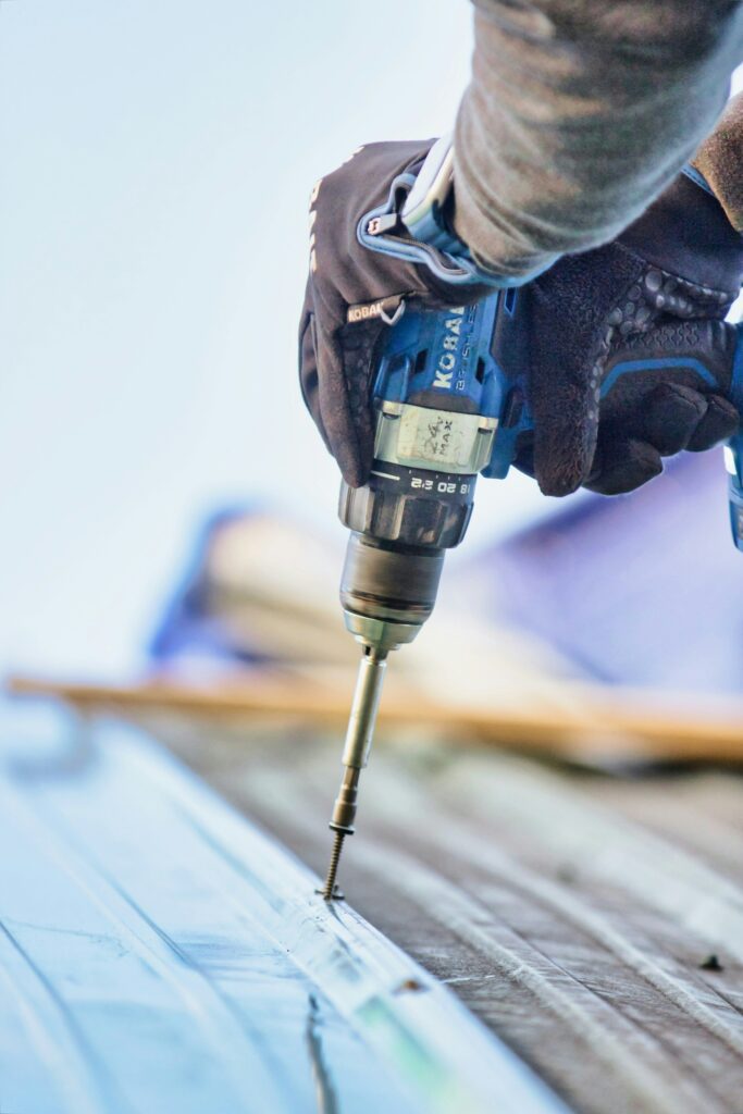 Close-up of a cordless drill driving a screw into roofing material