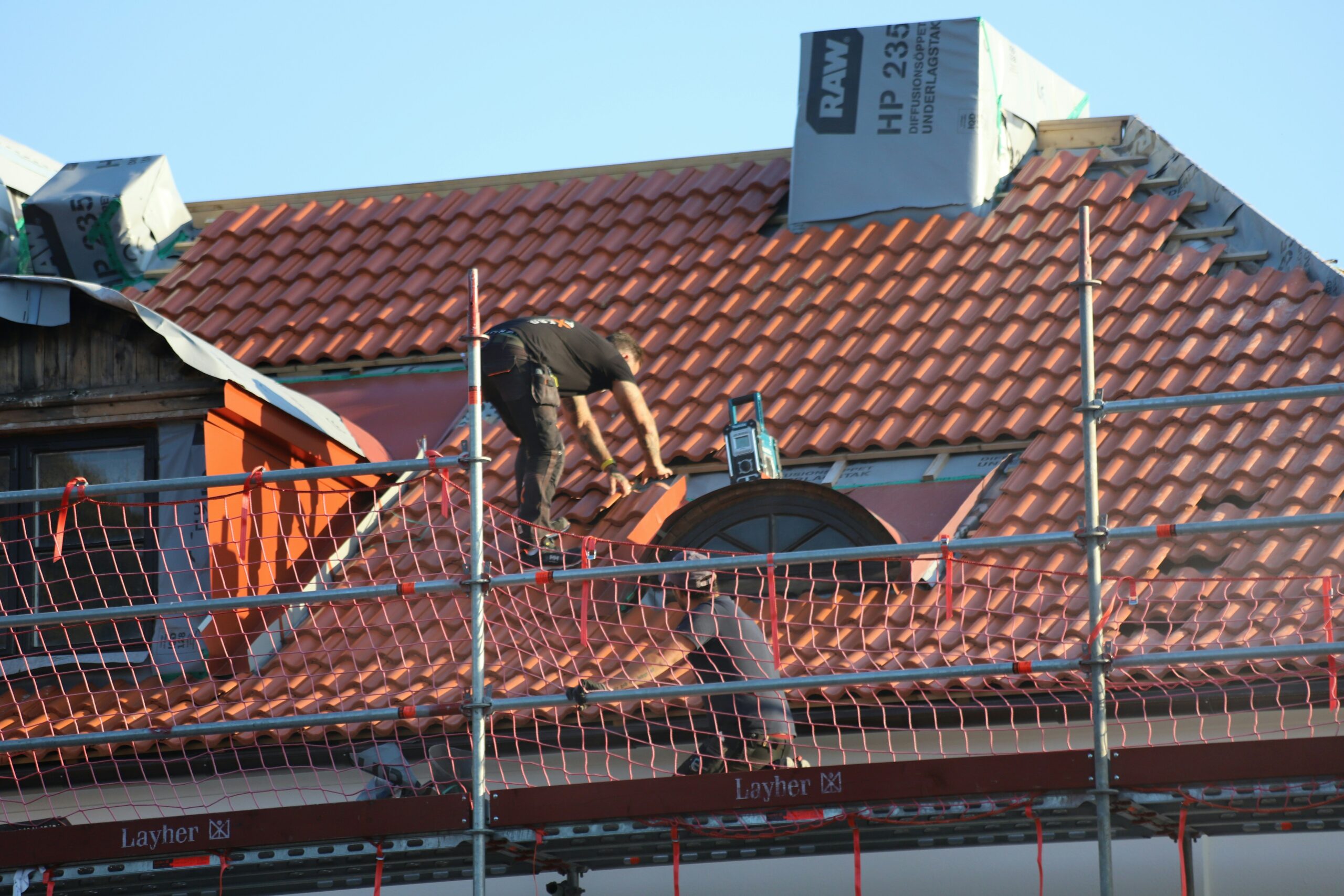 Roofers working on a red clay tile roof behind scaffolding Roofers working on a red clay tile roof behind scaffolding