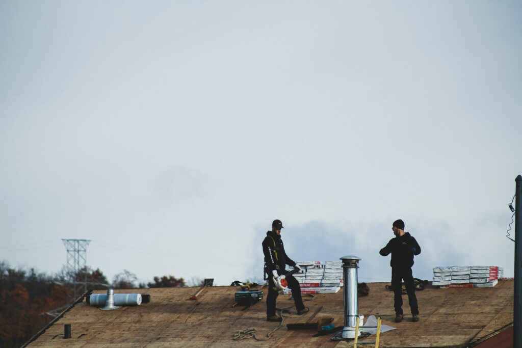 Two roofers working on a flat roof under an overcast sky Two roofers working on a flat roof under an overcast sky