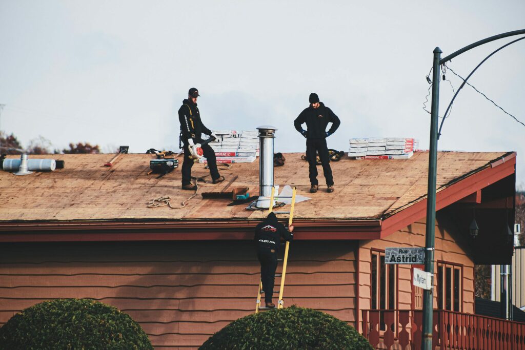Roofing crew on a low-slope house roof beside two chimneys Roofing crew on a low-slope house roof beside two chimneys