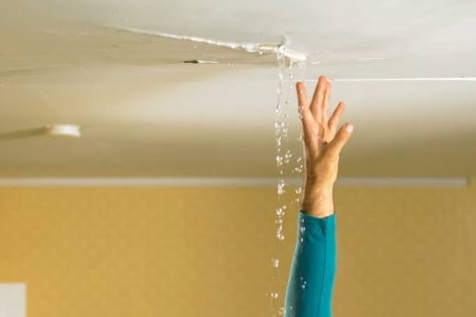 Water leaking through a cracked ceiling below a roof leak, with a hand reaching up