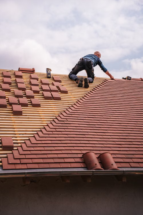 Roofer laying red clay tiles on a sloped roof