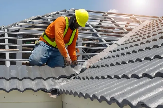 Roofer in a hard hat installing gray tile roofing over battens