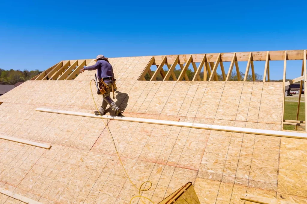 Roofer working on new roof sheathing beside exposed wooden trusses Roofer working on new roof sheathing beside exposed wooden trusses