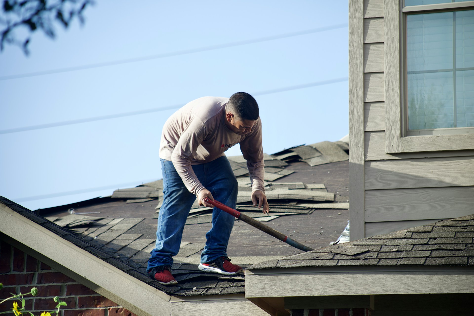 Roofer using a pry bar to remove worn asphalt shingles from a house roof