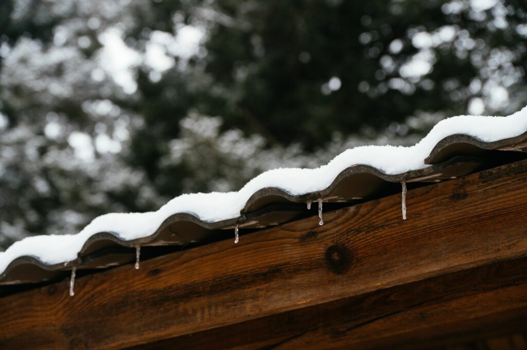 Snow and small icicles along the edge of a metal roof over wooden beams