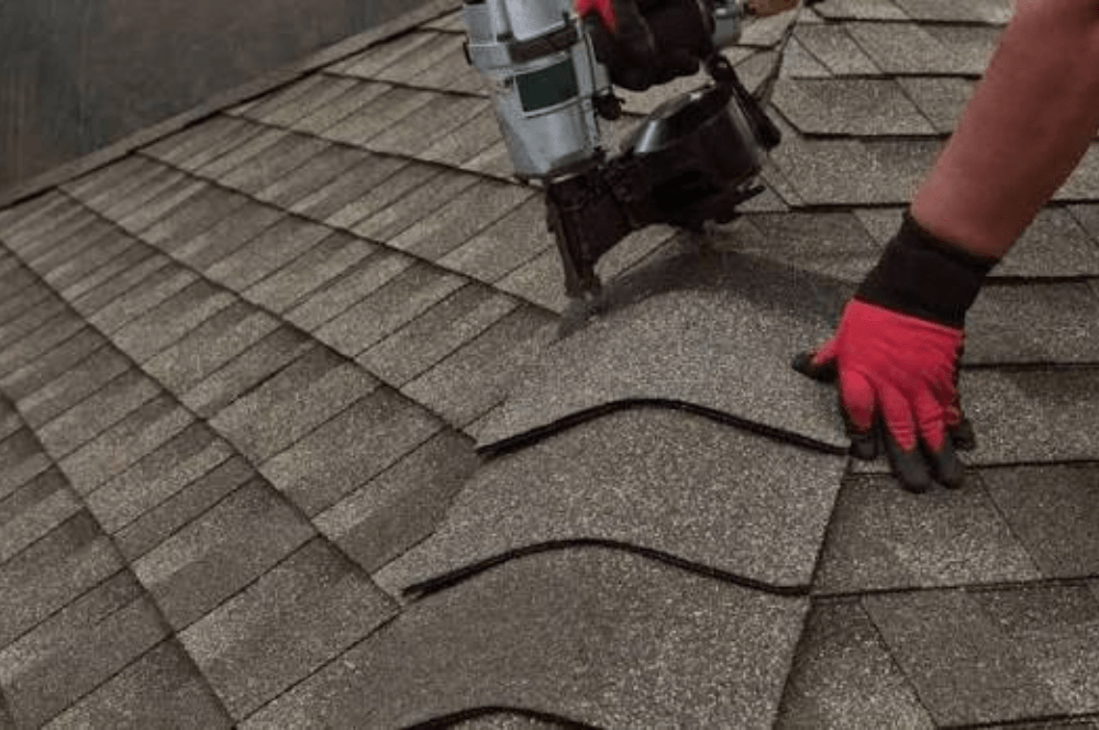 Roofer using a nail gun to fasten architectural asphalt shingles Roofer using a nail gun to fasten architectural asphalt shingles