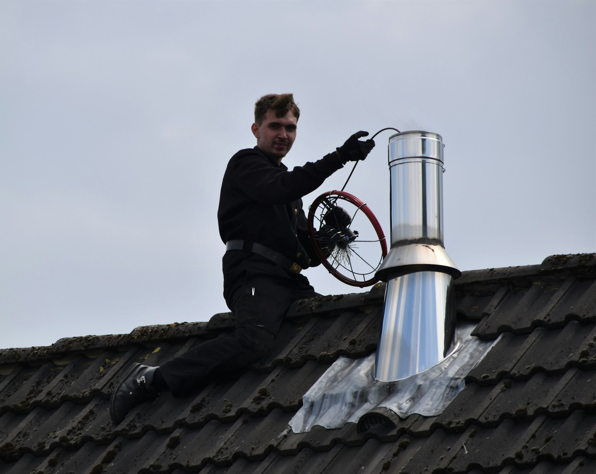 Roofer fitting a stainless steel chimney flue through a dark tile roof