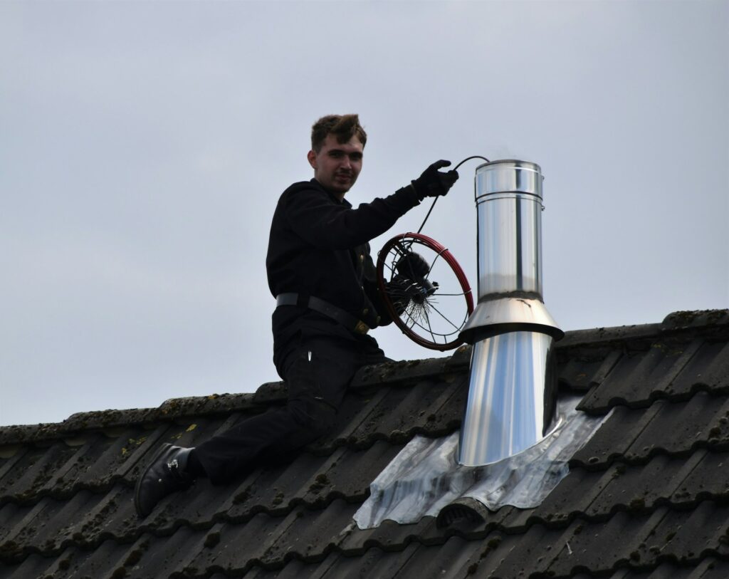 Worker on a tile roof installing a metal chimney flue pipe with flashing Worker on a tile roof installing a metal chimney flue pipe with flashing