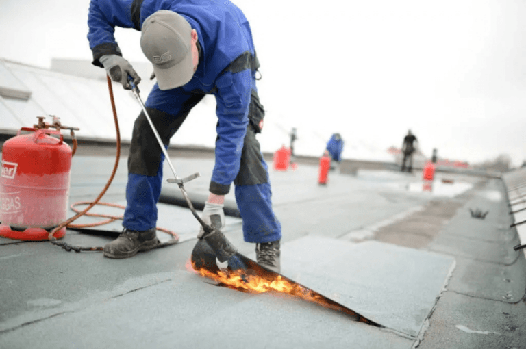 Roofer using a torch to repair membrane on a flat commercial roof Roofer using a torch to repair membrane on a flat commercial roof