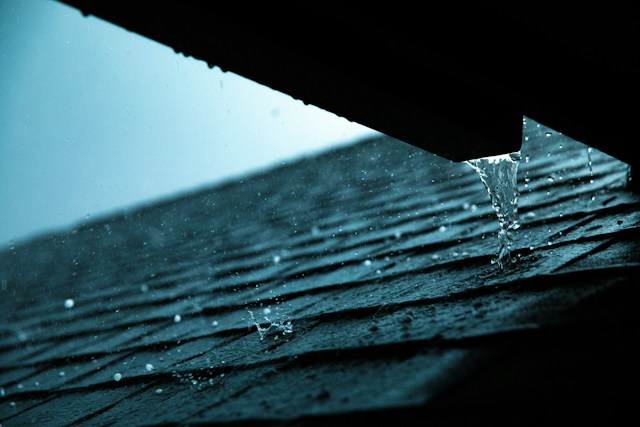 Rainwater dripping from a roof edge onto wet asphalt shingles