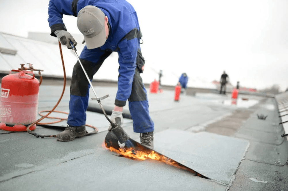 Roofer using a torch to repair membrane on a flat commercial roof Roofer using a torch to repair membrane on a flat commercial roof