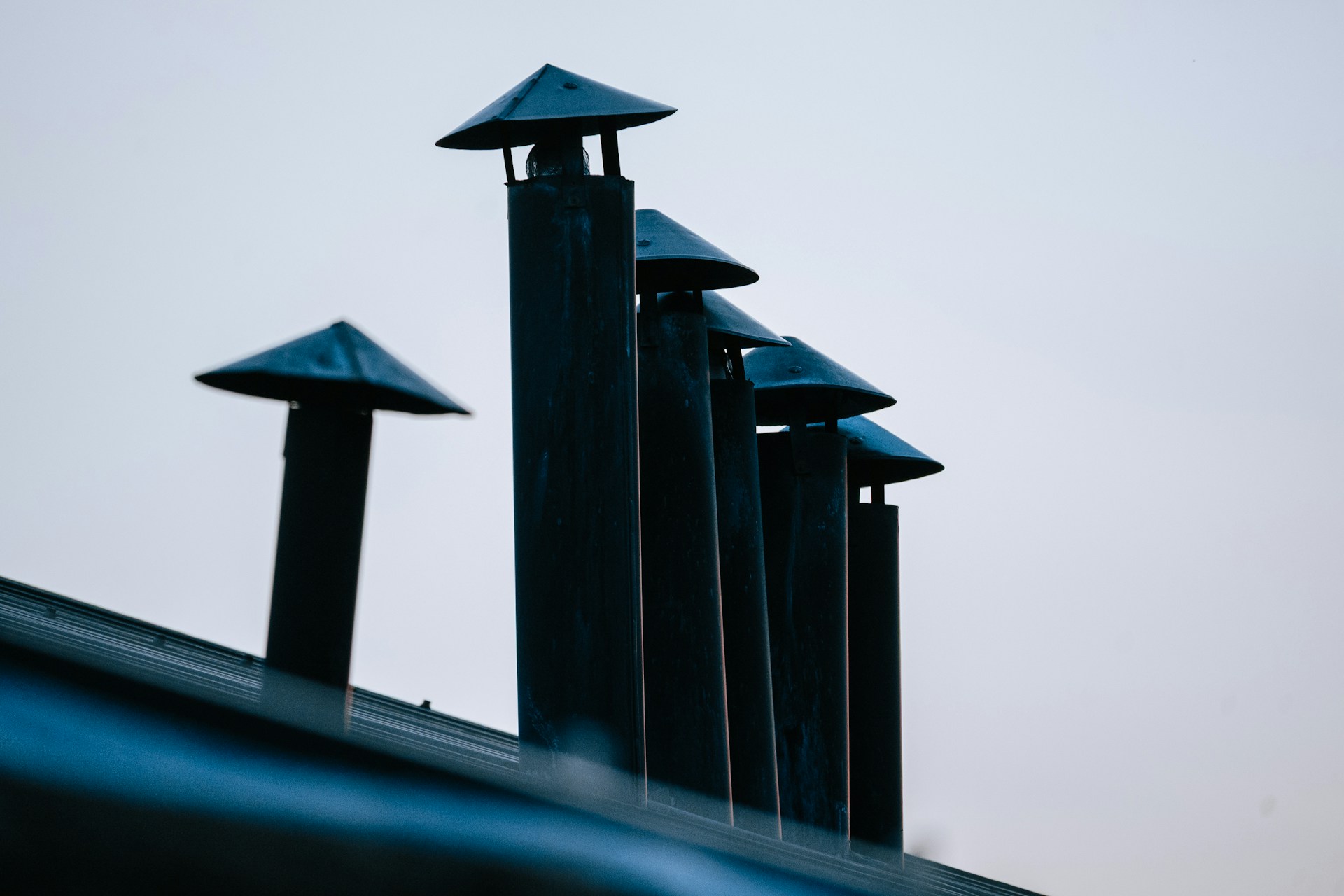 Row of metal chimney vent caps rising above a dark roof