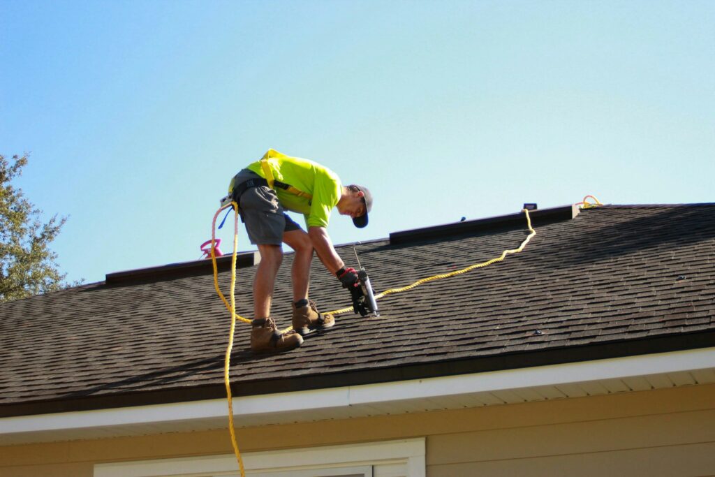 Roofer with a safety line working on a brown asphalt shingle roof Roofer with a safety line working on a brown asphalt shingle roof