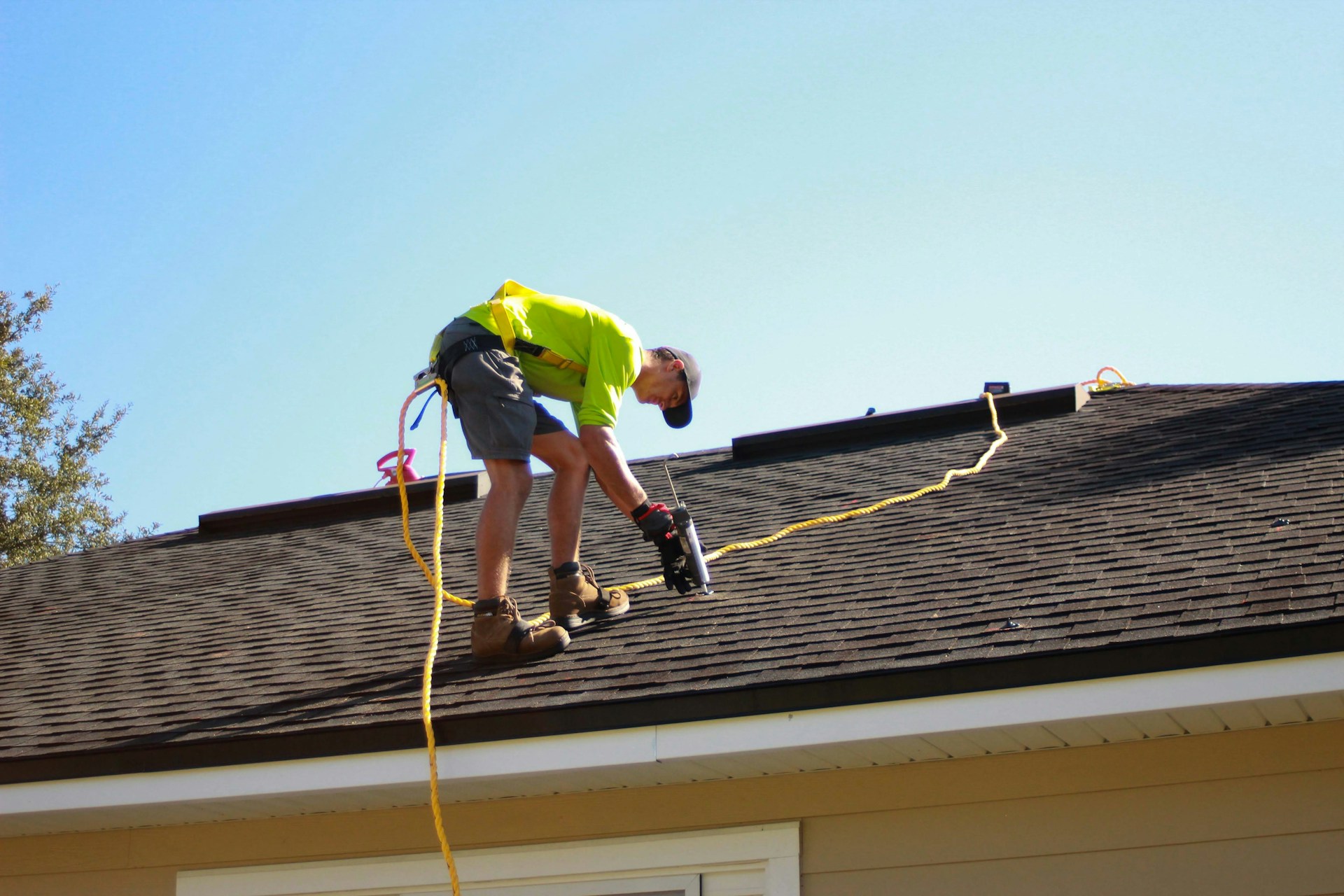 Roofer with a safety line working on a brown asphalt shingle roof Roofer with a safety line working on a brown asphalt shingle roof