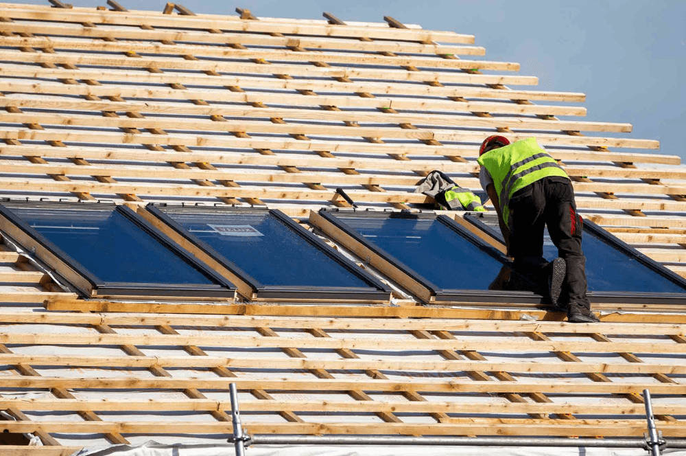 Roofer installing a row of skylight windows on a roof with exposed battens Roofer installing a row of skylight windows on a roof with exposed battens