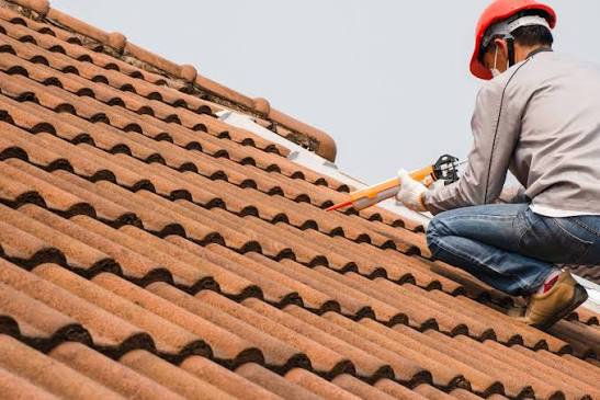 Roofer in a hard hat repairing a clay tile roof Roofer in a hard hat repairing a clay tile roof